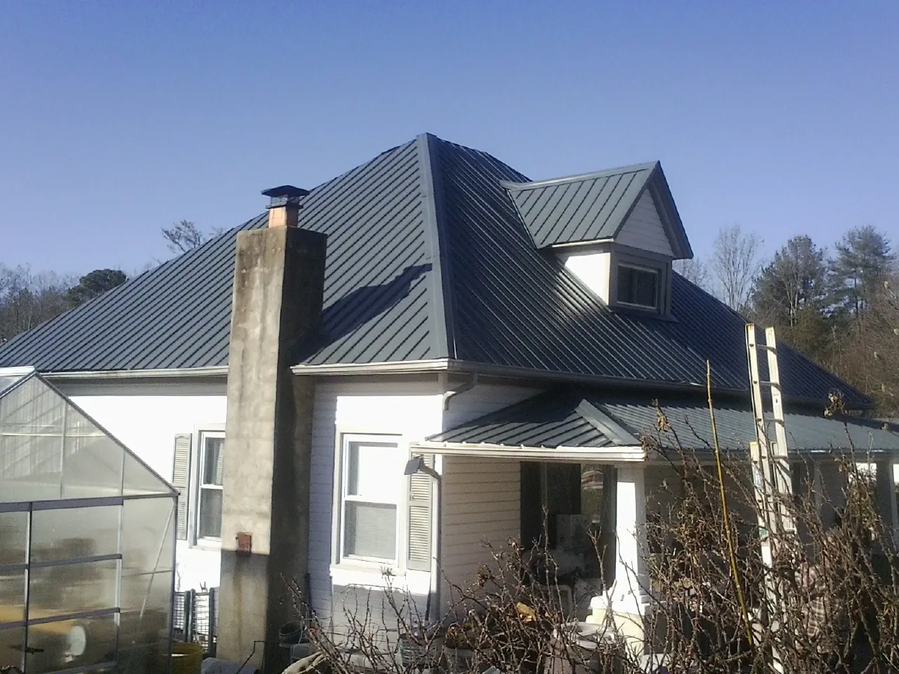Dark blue standing seam metal roof on a white farmhouse with dormer — Slate & Tile Roof Repair by Roofing Brothers in Faribault