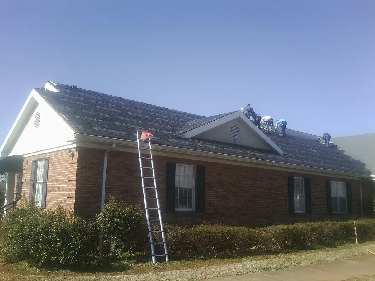 Crew tearing shingles off a brick ranch roof with a ladder set — Metal Roof Repair work by our crew in Faribault