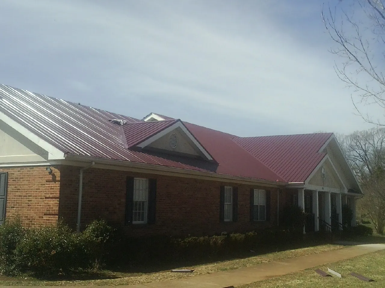 Red metal roof with gabled entries on a long brick building, from a Hail Damage Roof Repair job in Faribault