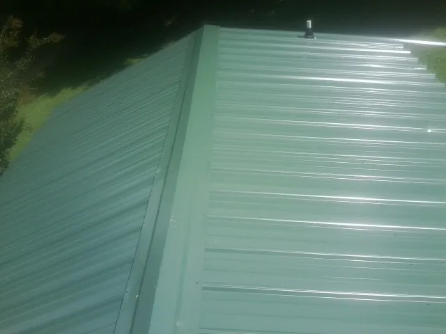 New green metal panels meeting at the ridge of a roof — Flat Roof Repair work by our crew in Faribault