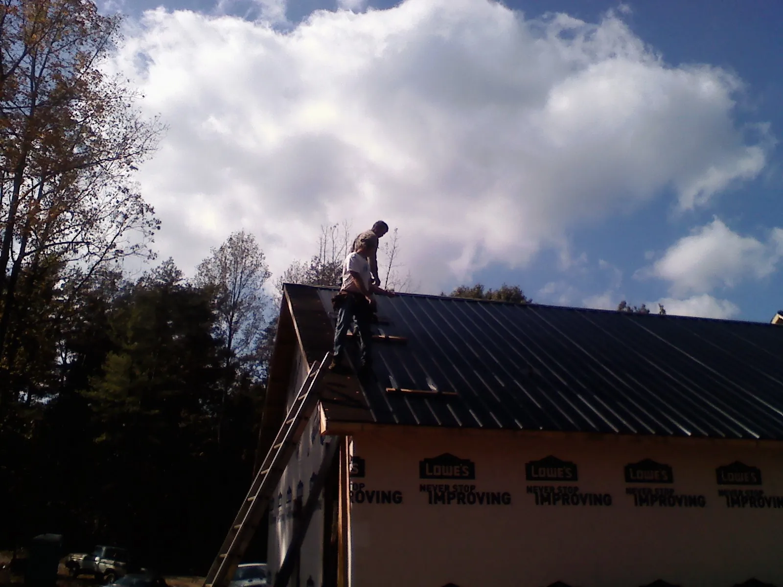 Roofer fastening dark metal panels high against a cloudy sky, from a Roof Inspection job in Faribault
