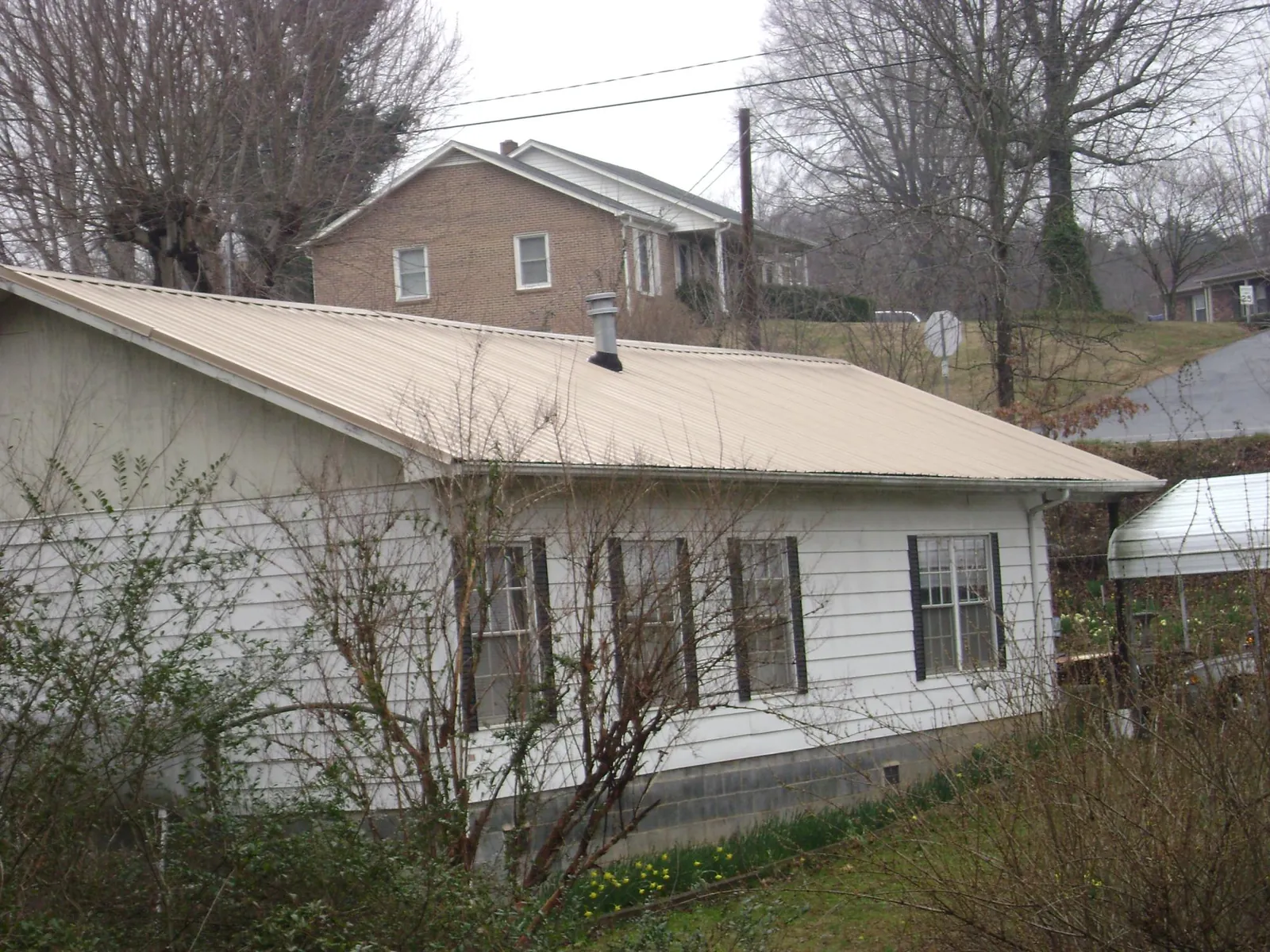 Tan metal roof on a white sided house set into a hillside — Commercial Roofing by Roofing Brothers in Faribault