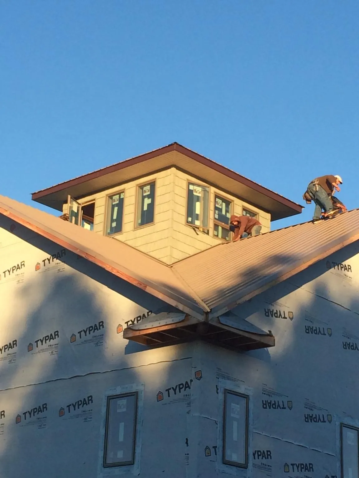 Roofers working around a rooftop cupola on a new metal roof at sunset — Roof Waterproofing in Faribault by Roofing Brothers